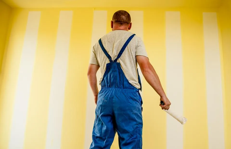 Decorator applying paint with a roller to a freshly striped wall